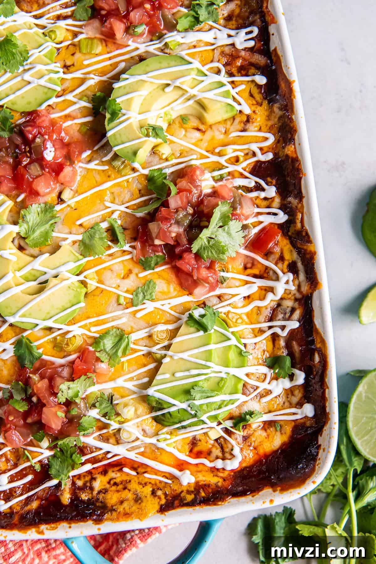 A top down closeup shot of chicken enchilada casserole topped with sour cream and sliced avocado.