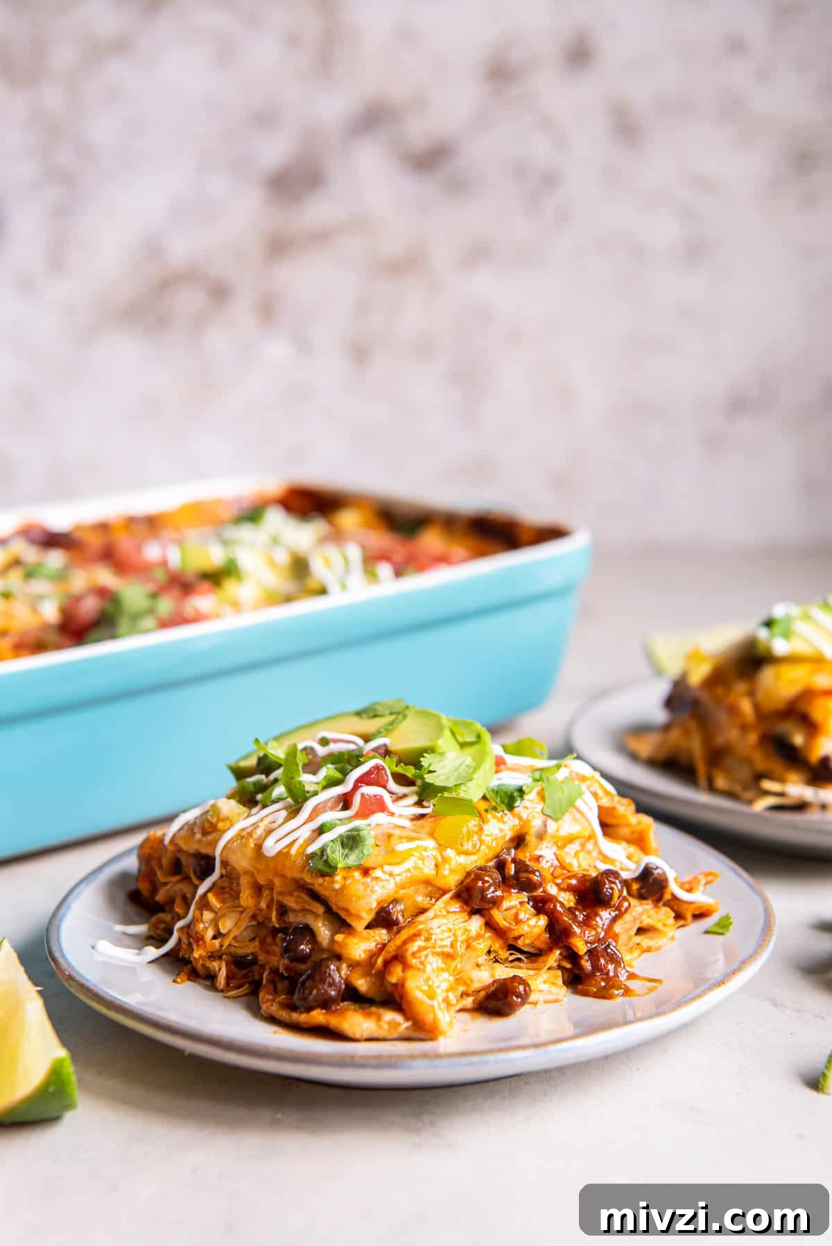 A serving of chicken enchilada casserole on a white plate with a blue casserole dish in the background.