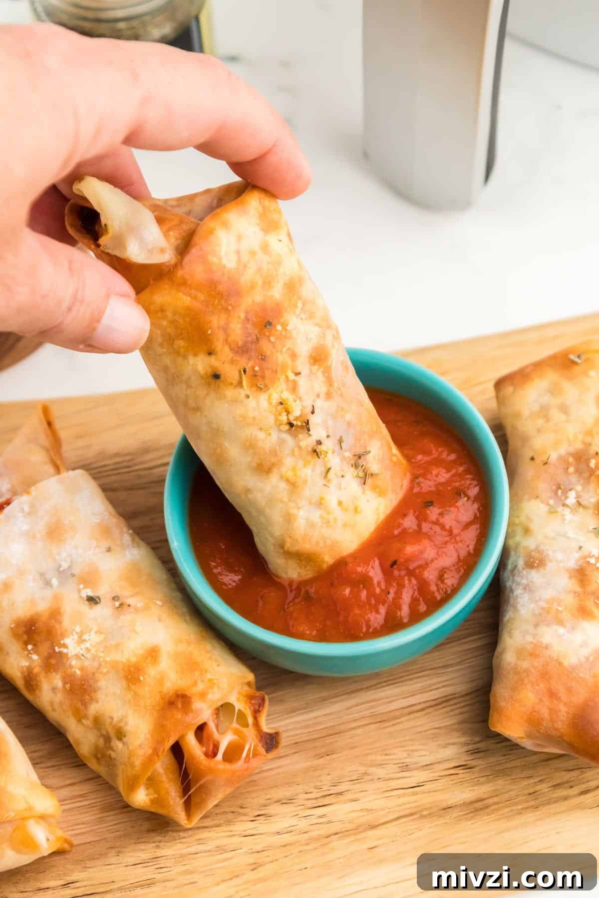 A egg roll with pizza filling dipping into a bowl of marinara sauce.