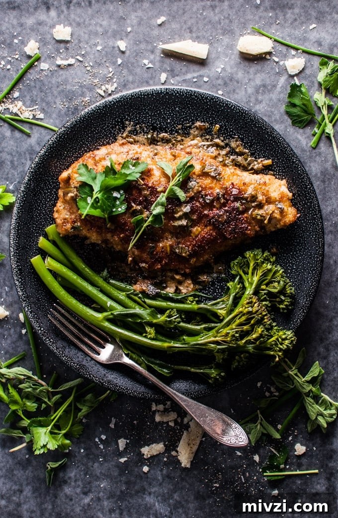 Parmesan Crusted Chicken with Fresh Herb Sauce 2 parmesan crusted chicken breasts with a fresh herb sauce on a plate with broccolini and a fork