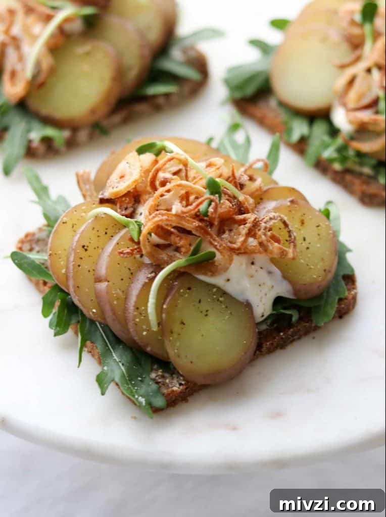 An open sandwich with sliced potato, arugula and crispy shallots on a plate