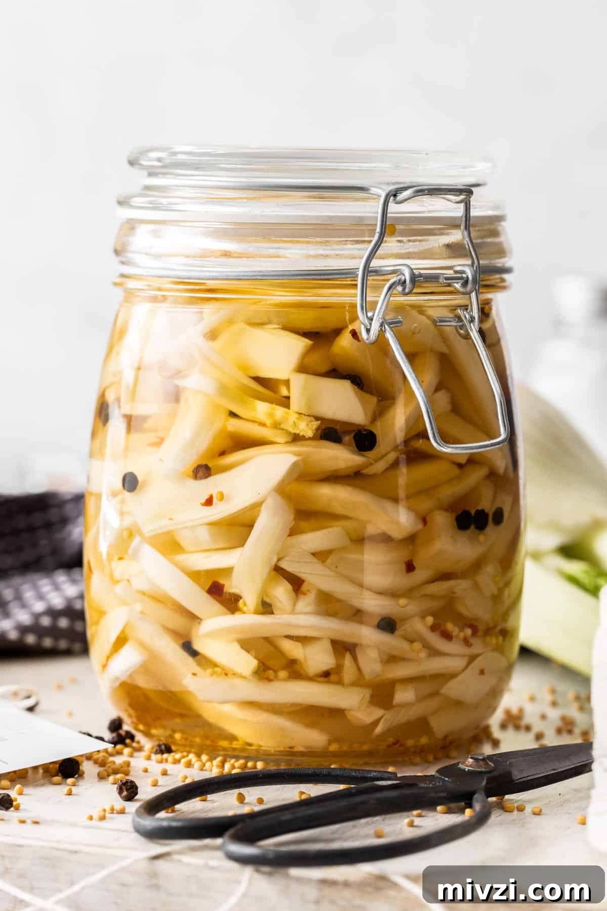 Jar of Pickled Fennel, sitting on a wooden board, with some herbs and spices around the edge.