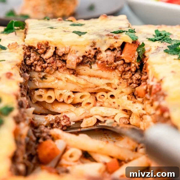 Someone lifting out a square of Greek pastitsio with 3 layers