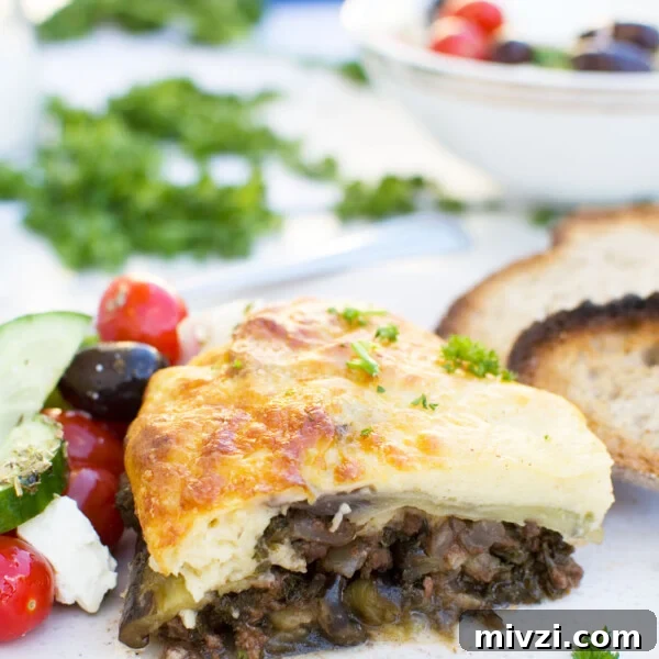 A piece of easy moussaka on a white plate with bread and Greek salad