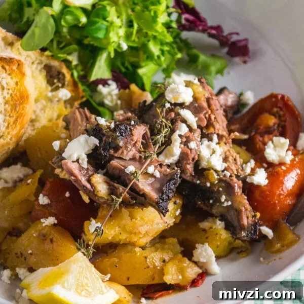 Closeup of a dish of slow roasted Greek lamb in a white dish with colourful garnishes such as feta and lettuce
