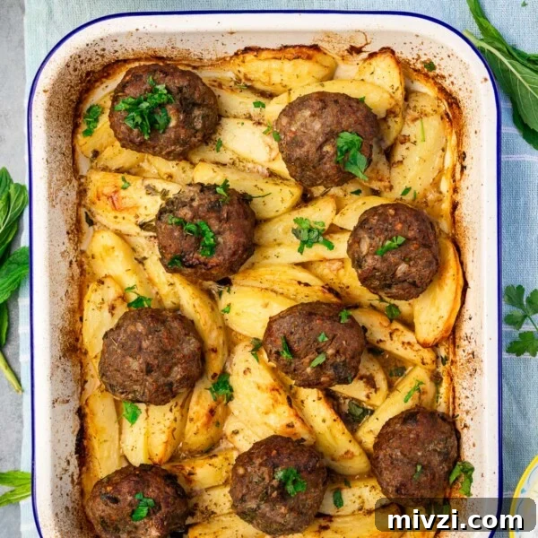 Overhead of Greek biftekia or hamburgers on top of lemon potatoes in a blue-rimmed white baking pan