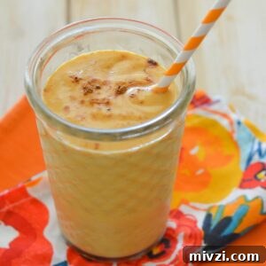 A thick and creamy pumpkin smoothie in a tall glass with a straw.