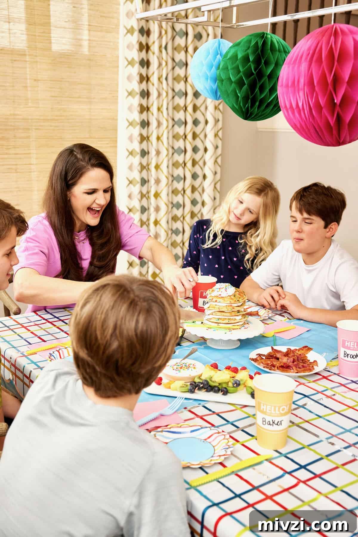 A family of a mother and four kids enjoying breakfast on the first day of school with colorful hanging paper decorations in the background.