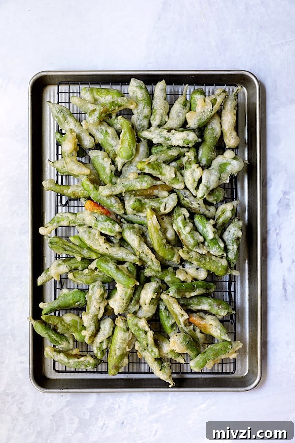 Crispy Beer-Battered Shishito Tempura with Spicy Garlic Dipping Sauce 10 Photo of fried peppers on rack set over rimmed baking sheet.