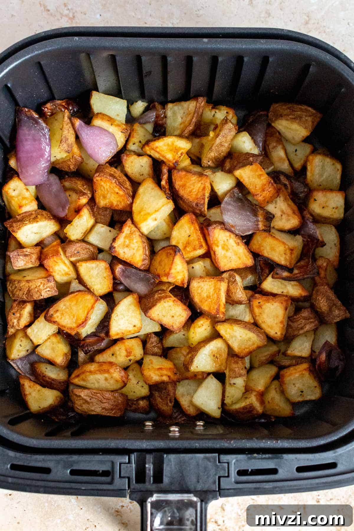 A close up view of potatoes and onions in an air fryer basket.