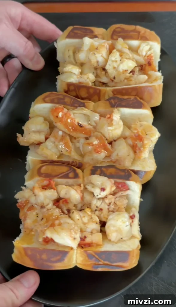 Spicy Hot Honey Lobster Rolls with Chili Crisp 11 Three hot honey butter lobster rolls with chunks of lobster meat on golden brioche buns served on black plate