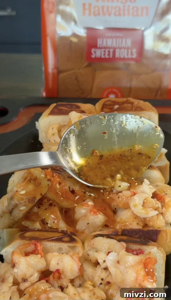 Spicy Hot Honey Lobster Rolls with Chili Crisp 3 Hot honey butter lobster rolls with golden sauce being drizzled from a spoon, Hawaiian sweet rolls in background