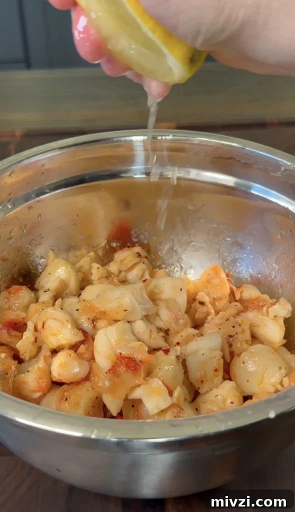 Spicy Hot Honey Lobster Rolls with Chili Crisp 10 Fresh lobster meat seasoned with spices in a stainless steel mixing bowl, being drizzled with sauce