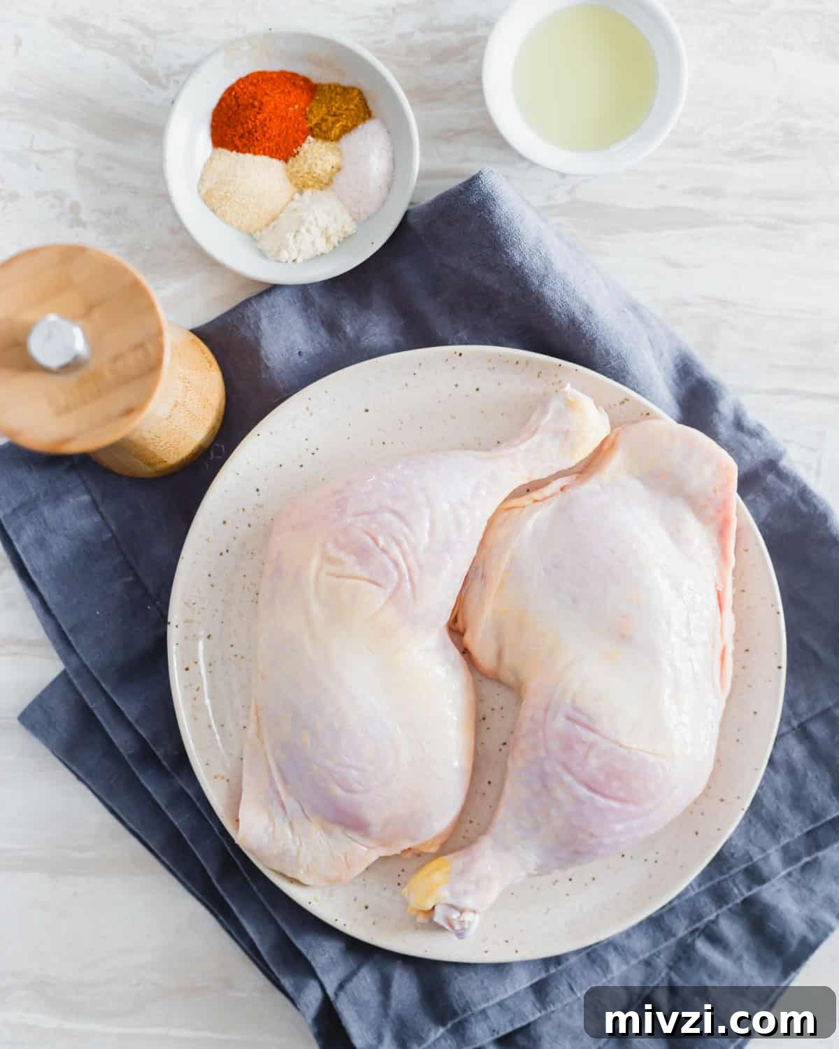 Raw chicken leg quarters on a plate with spice rub and oil to the side. Raw chicken leg quarters on a plate with spice rub and oil to the side.