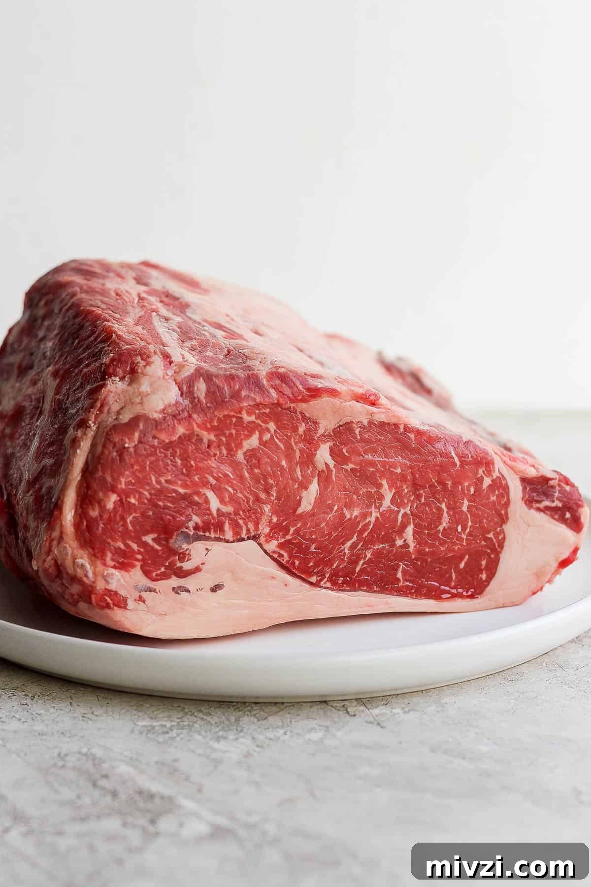 Raw prime rib roast on a white plate.