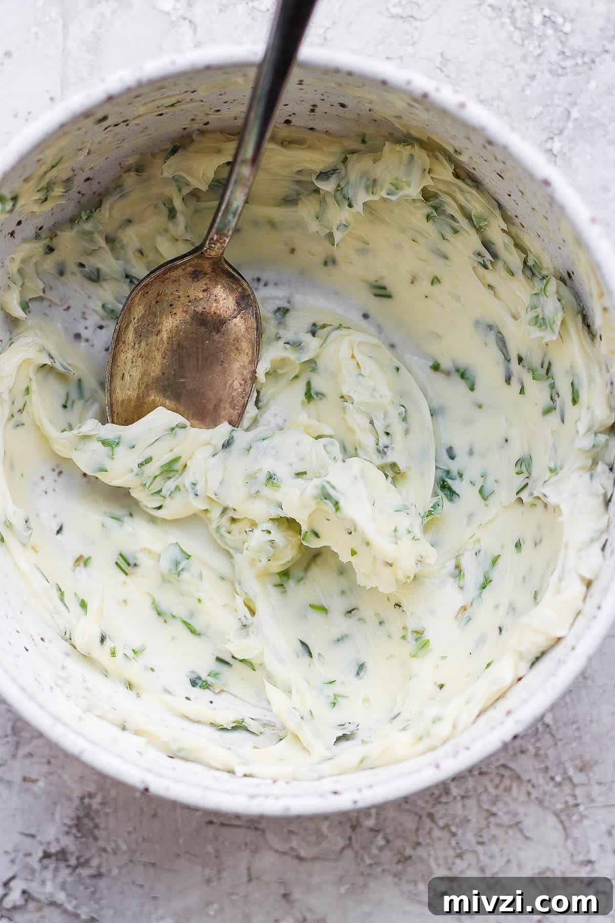 A bowl of herbed butter in a bowl with a spoon.