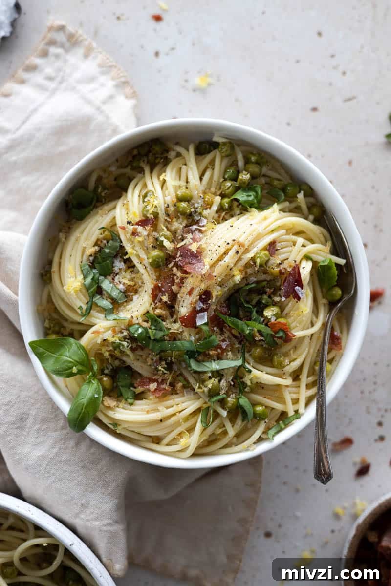A bowl of spring pasta with lemon, peas and prosciutto with a spoon and a cream colored linen. 