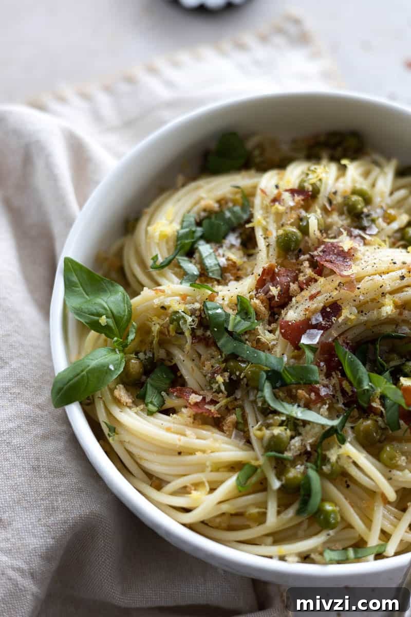 A closeup of pasta with peas and prosciutto in a white bowl.