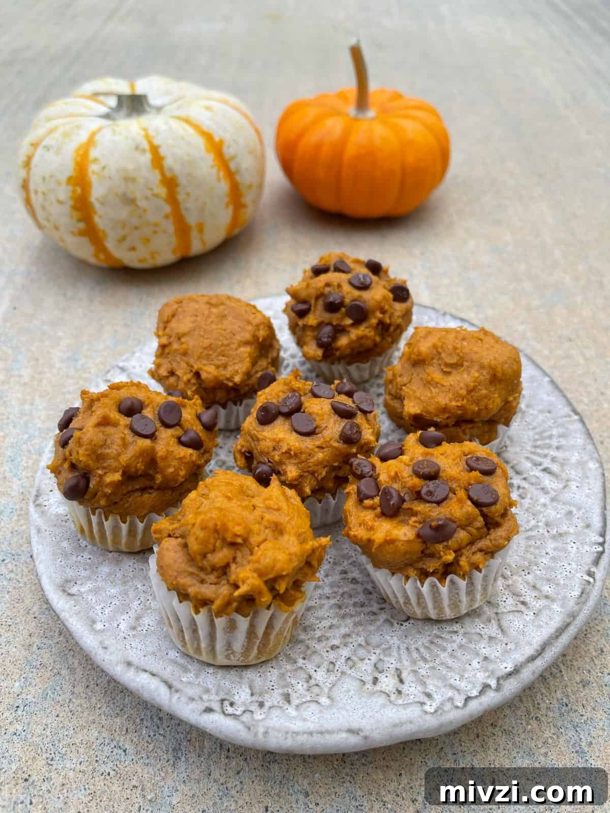 Pumpkin Spice Muffins Made from Cake Mix (Weight Watchers-Friendly) 2 Fresh baked pumpkin spice cake mix mini muffins on small ceramic plate with two small pumpkins in the background.