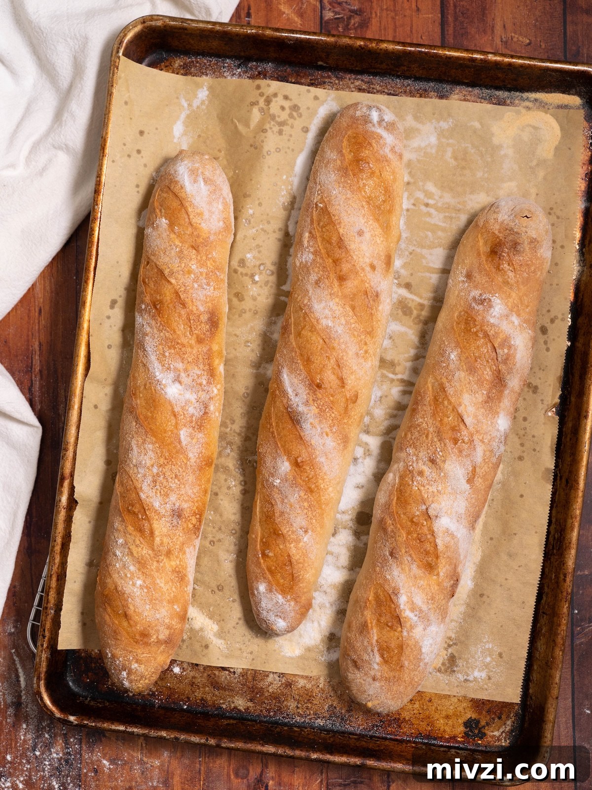 How to Make Classic Sourdough Baguettes at Home 2 Three sourdough demi baguettes freshly baked on a baking sheet