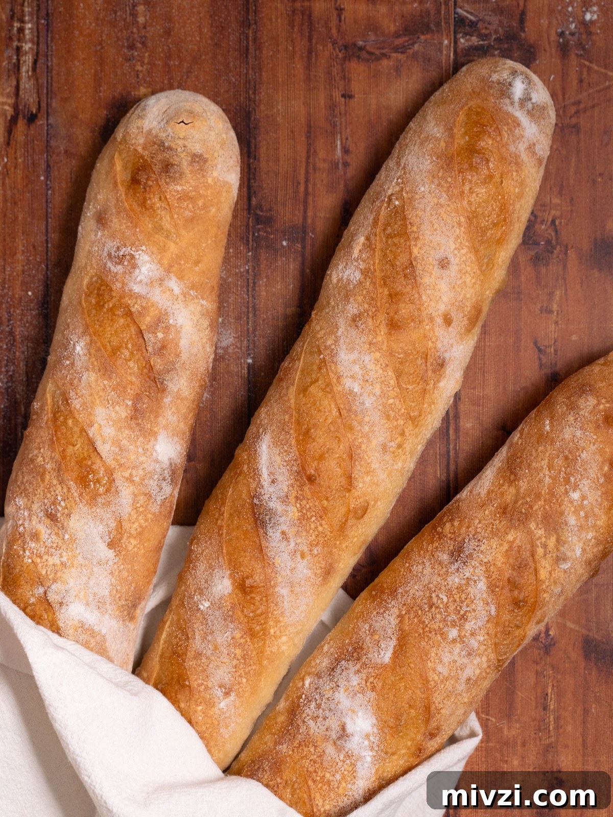 How to Make Classic Sourdough Baguettes at Home 3 Three sourdough demi baguettes, baked and wrapped in a tea towel