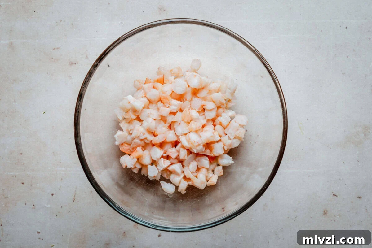 A glass bowl filled with small, diced pieces of shrimp sits on a light-colored countertop.