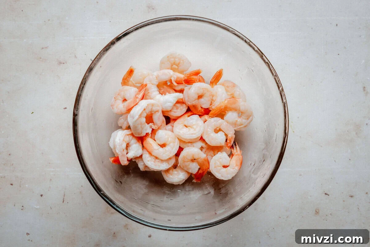 A glass bowl filled with cooked, peeled shrimp is placed on a light-colored countertop.