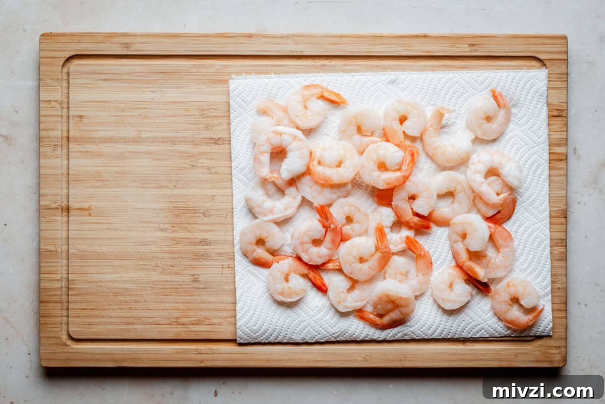 Cooked shrimp arranged on a white paper towel on a wooden cutting board, ready for preparation or serving.
