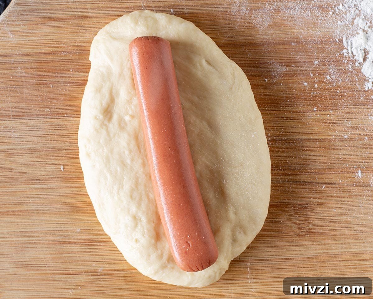 Rolling the dough into an oval and placing hotdog on it.