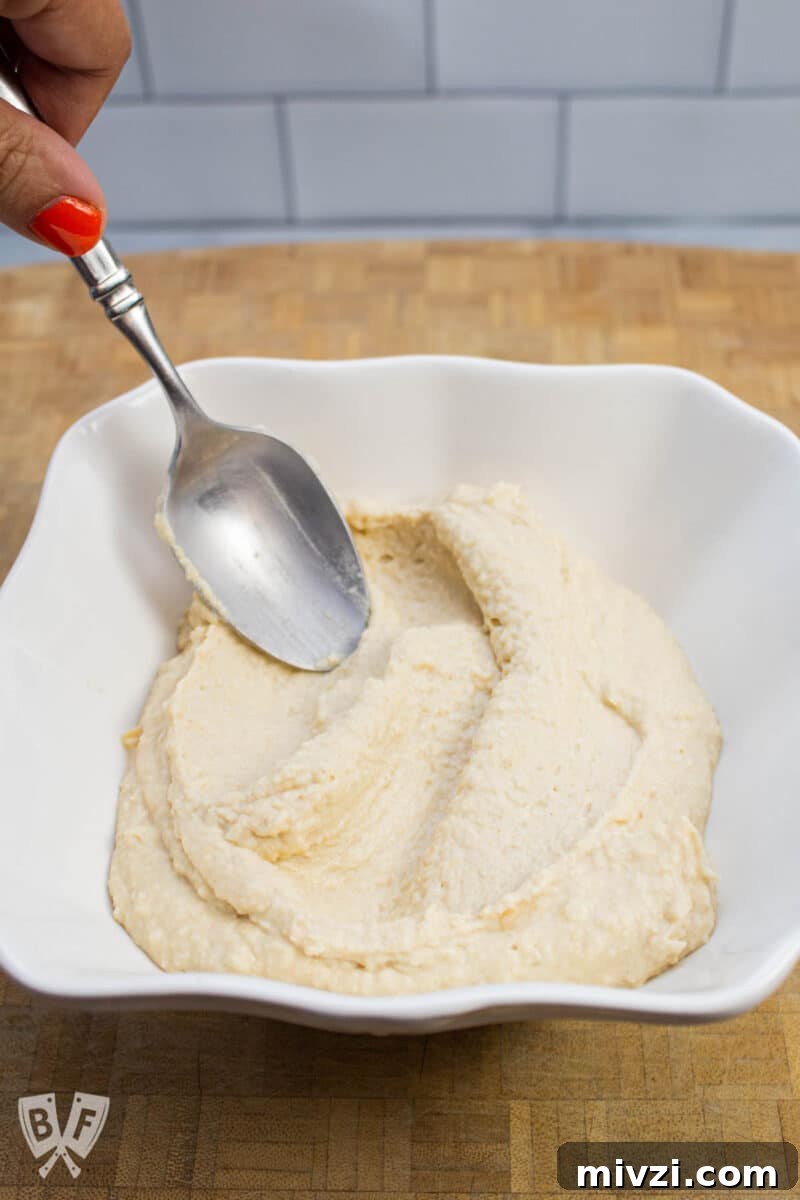 Classic Hummus from Canned Chickpeas – Quick Authentic Recipe 15 Smoothing hummus into a bowl with a spoon.