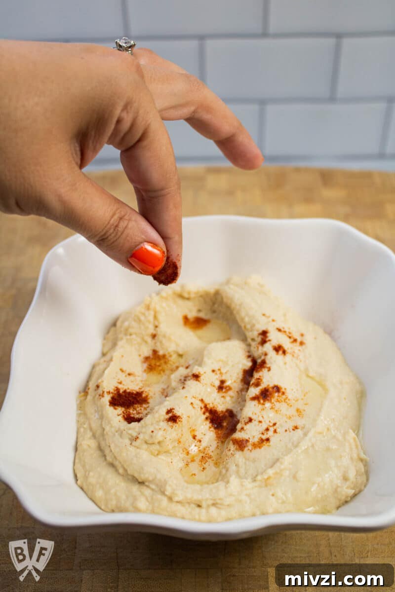 Classic Hummus from Canned Chickpeas – Quick Authentic Recipe 16 Sprinkling paprika onto a bowl of hummus.