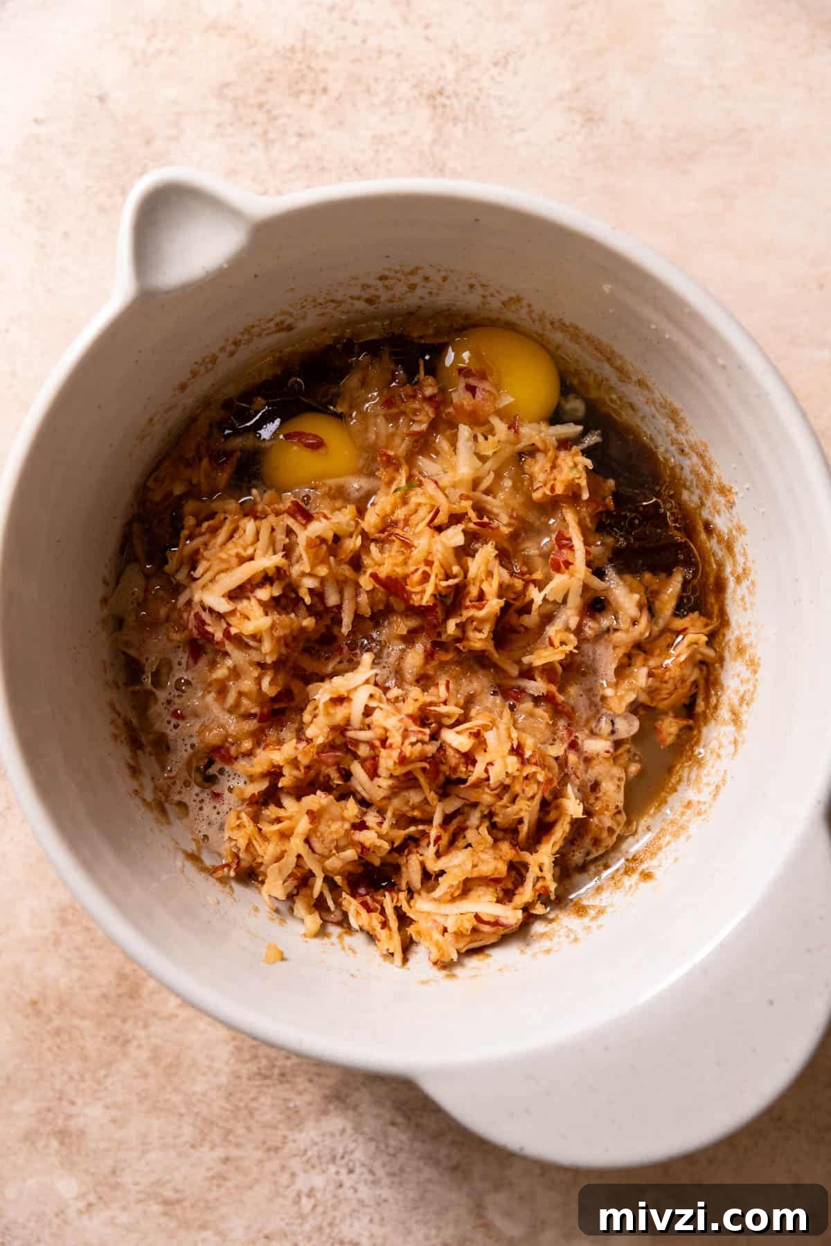 A mixing bowl with the wet ingredients, shredded apples, and apple juice before mixing.