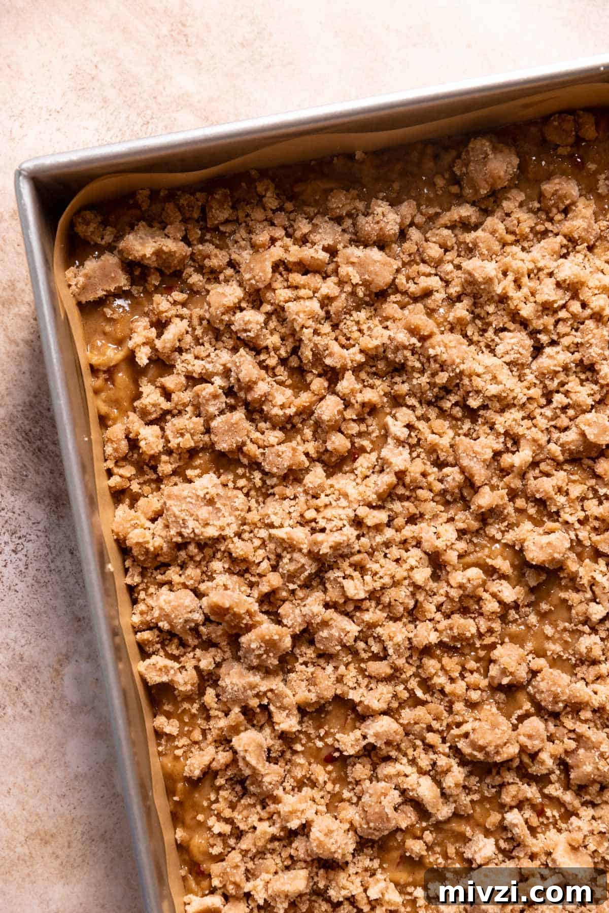 A baking pan with the apple cake batter and cinnamon crumbs on top before baking.