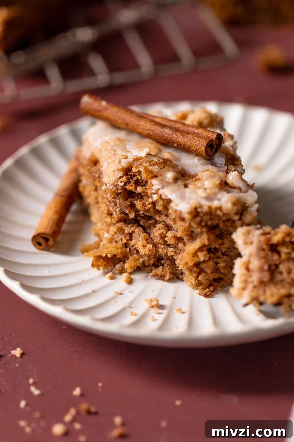 a slice of apple cake on a plate with a stick of cinnamon on top.