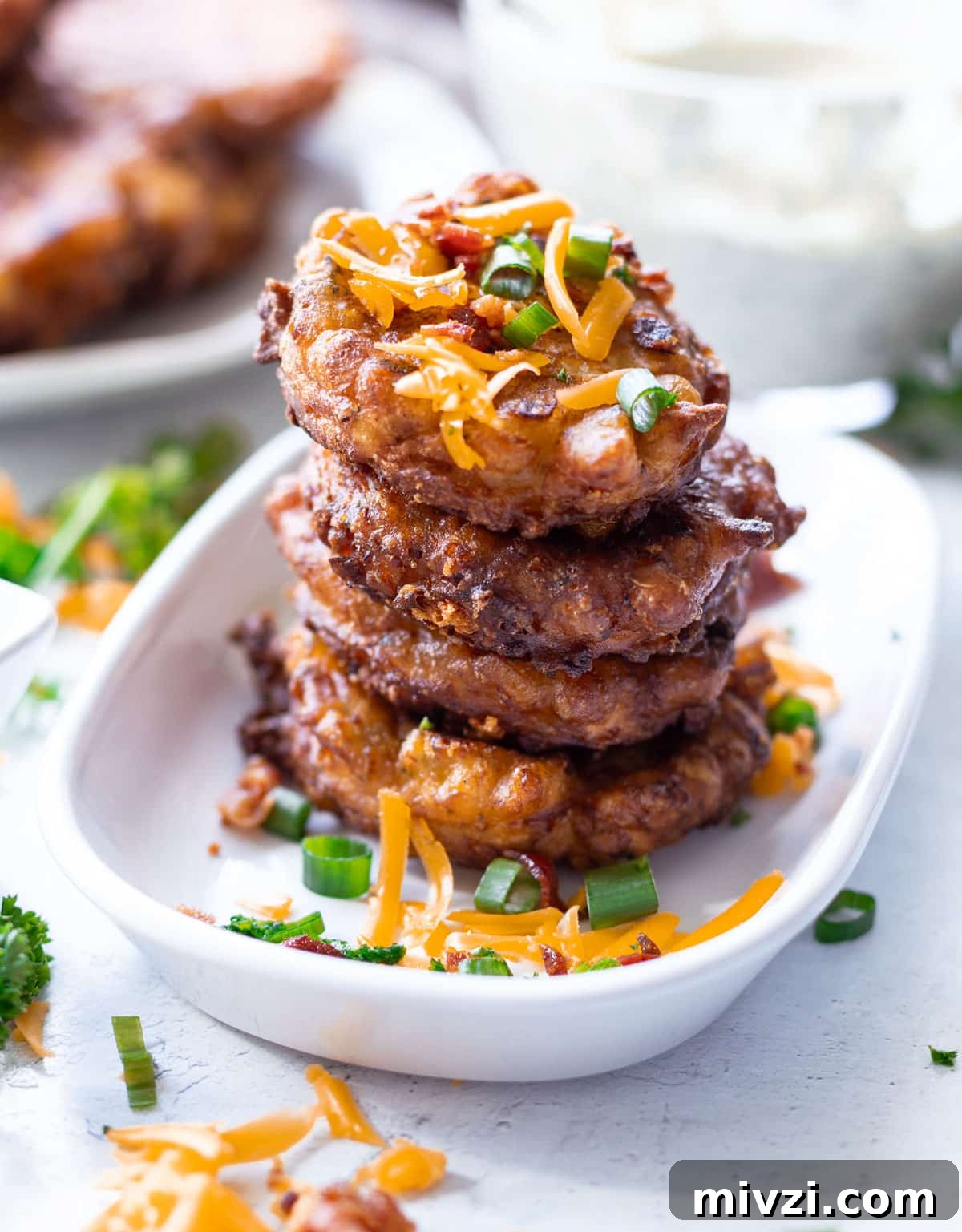 Stacked corn fritters on a plate covered with bacon, cheese and scallions.