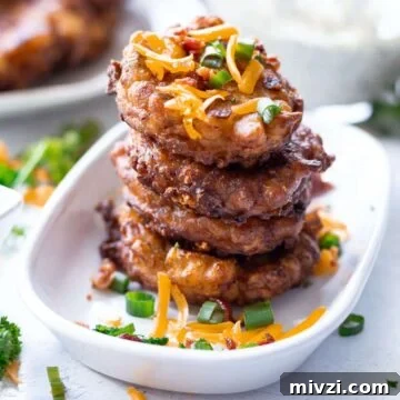 Stacked fried corn fritters in a dish topped with bacon, scallions, and cheese.