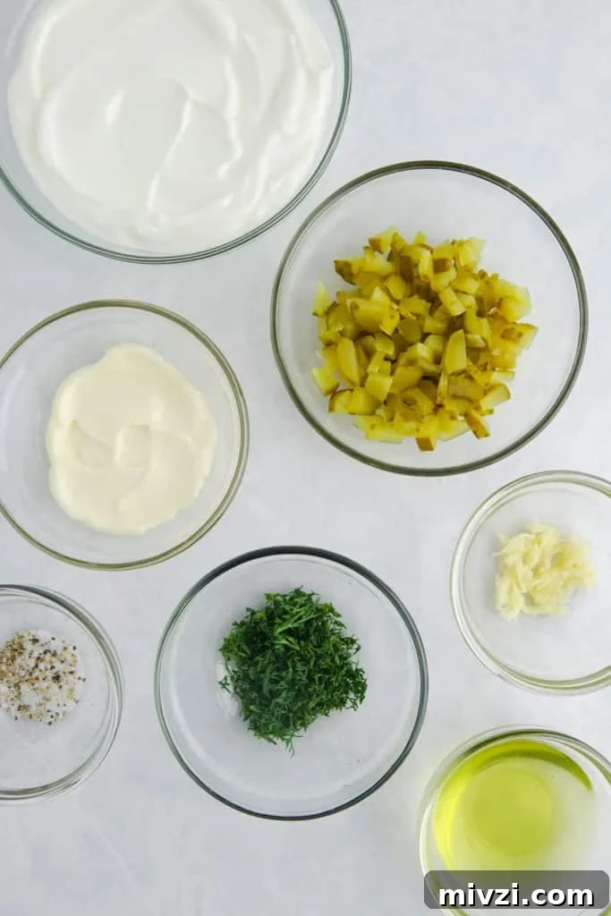 Ingredients for greek yogurt dill dip displayed in glass bowls on a white marble counter; greek yogurt, mayonnaise, chopped pickles, minced garlic, fresh dill, pickle juice, salt and pepper.