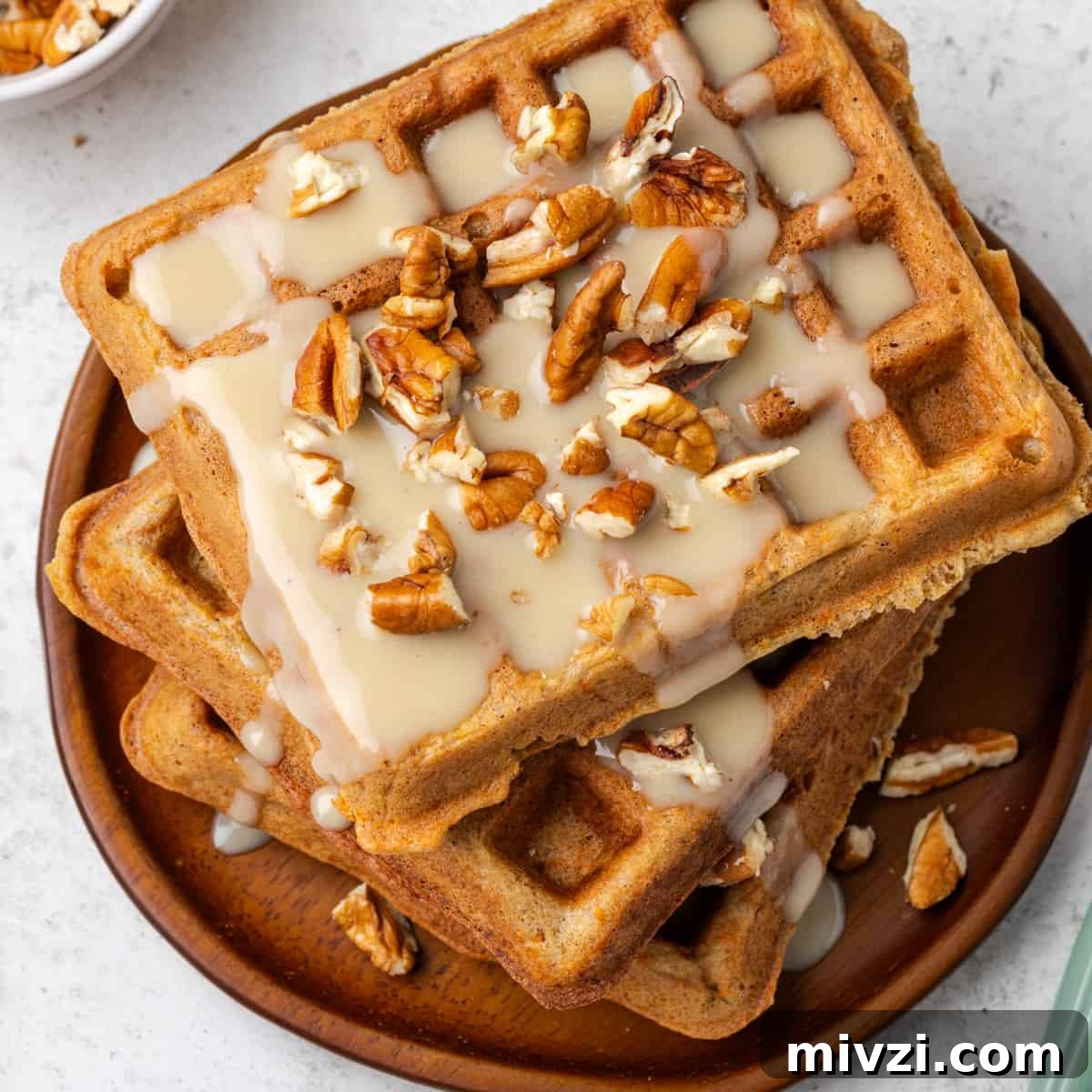 A stack of carrot cake waffles topped with maple cream cheese syrup and chopped nuts.