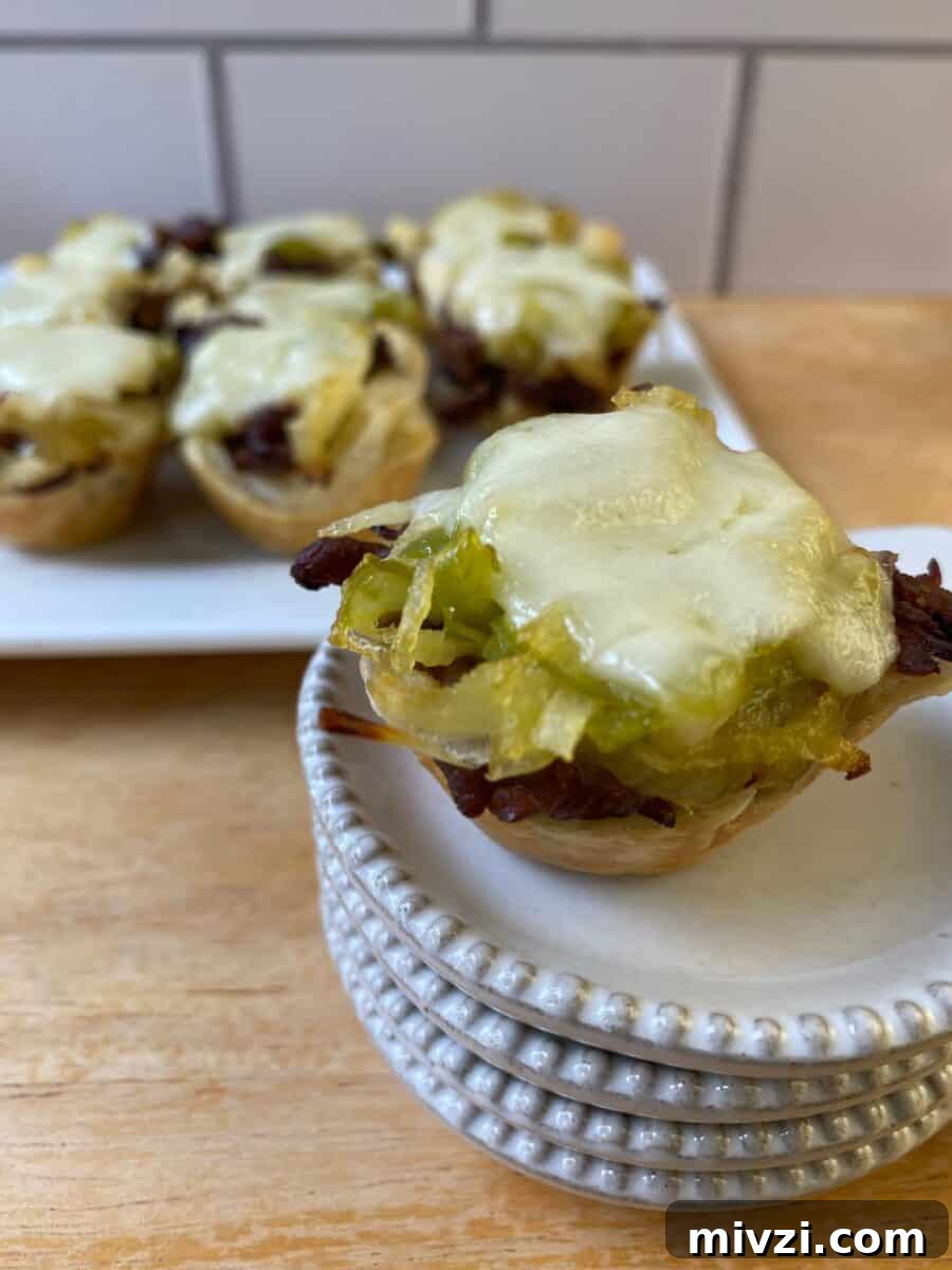 Mini Philly Cheesesteak Sliders: Bite-Sized Steak & Cheese Delight 2 Philly Cheesesteak bite on a small stack of dishes with the serving plate in the background.