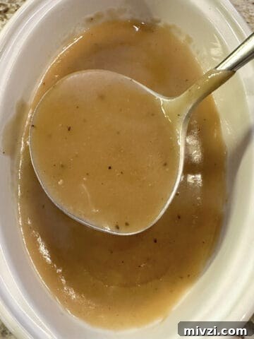 A gravy bowl full of gravy with a serving spoon.