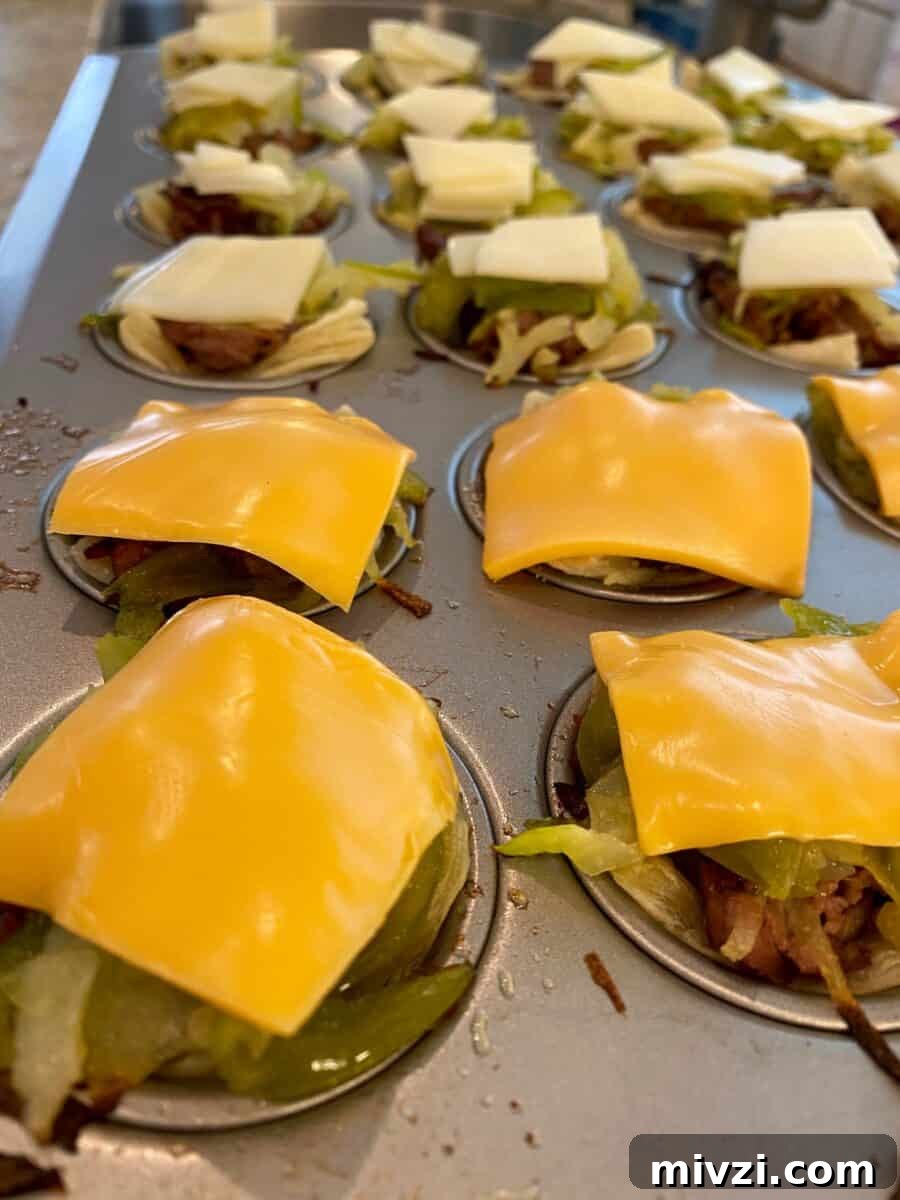 Mini Philly Cheesesteak Sliders: Bite-Sized Steak & Cheese Delight 4 Mini Philly Cheesesteaks in a mini-muffin pan with melted cheese on top of each one.