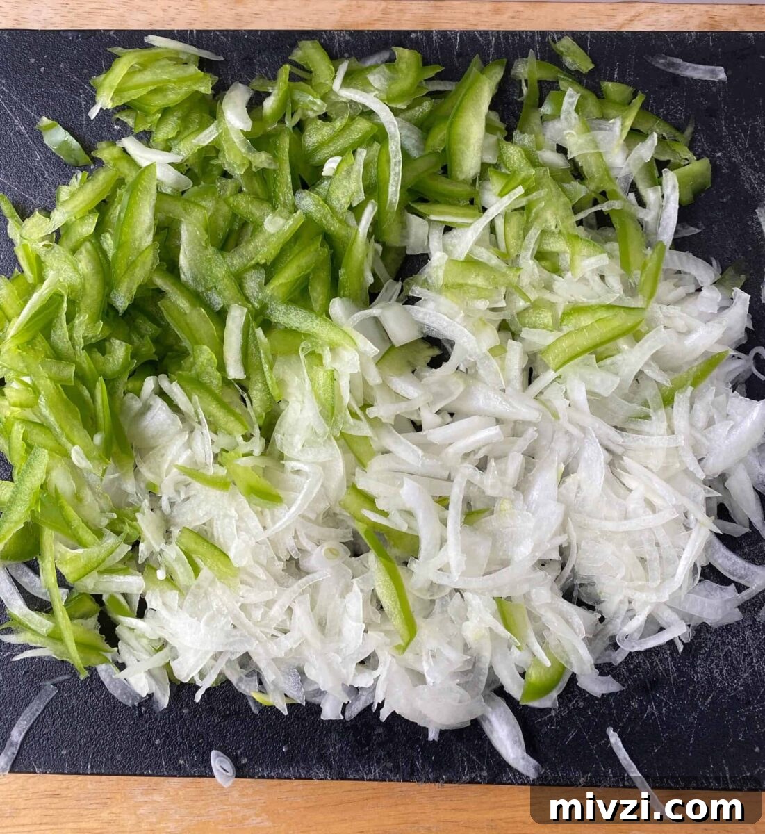 Mini Philly Cheesesteak Sliders: Bite-Sized Steak & Cheese Delight 7 Sliced green pepper and onion on a cutting board.
