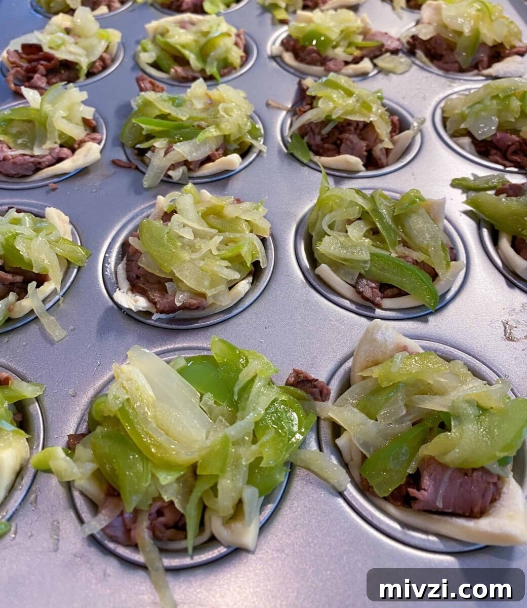 Mini Philly Cheesesteak Sliders: Bite-Sized Steak & Cheese Delight 8 Mini Philly Cheesesteaks in a mini-muffin pan with cooked veggies on top of each one.