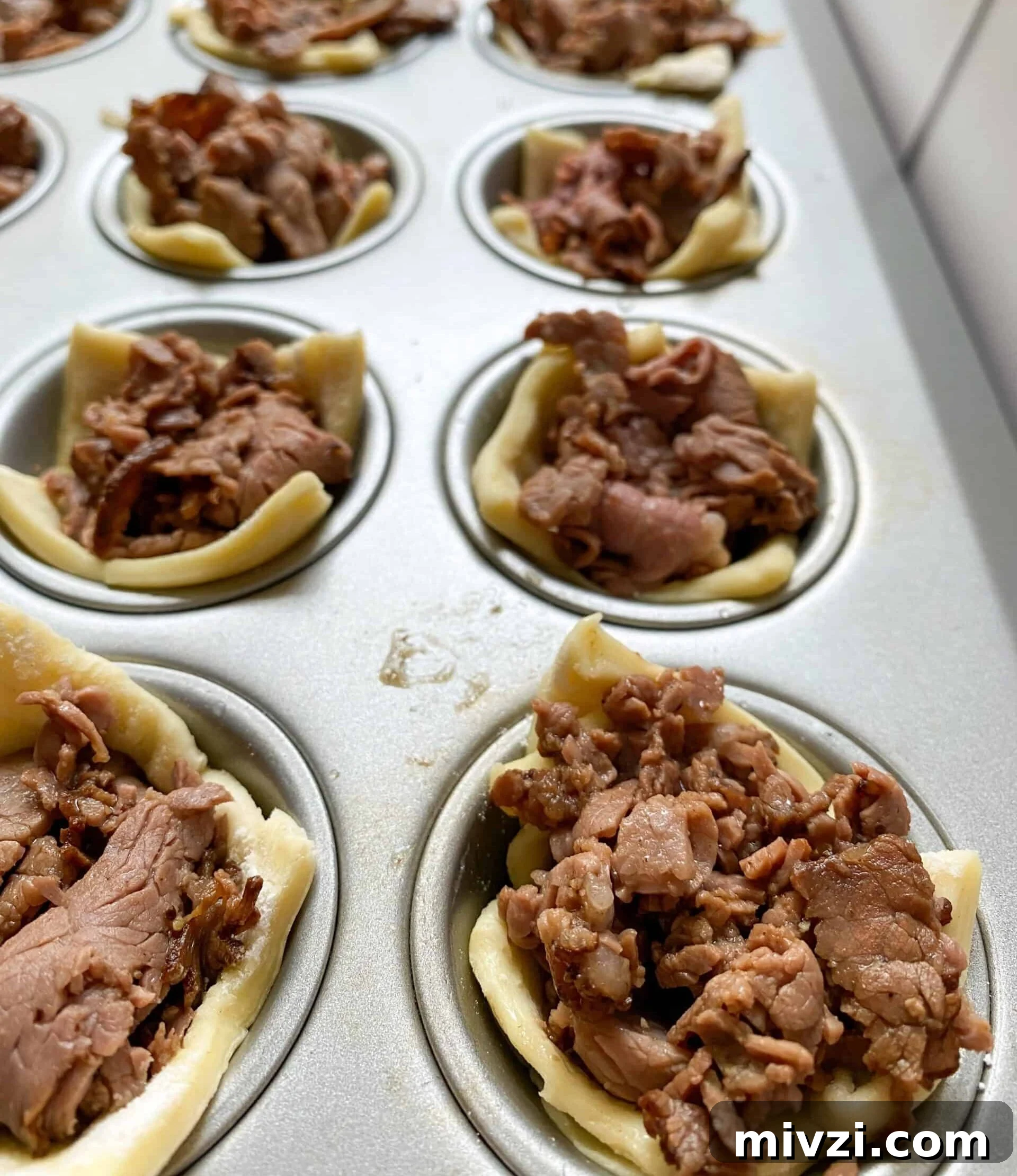 Mini Philly Cheesesteak Sliders: Bite-Sized Steak & Cheese Delight 10 Mini muffin cups with cooked roast beef and puffed pastry in each one.