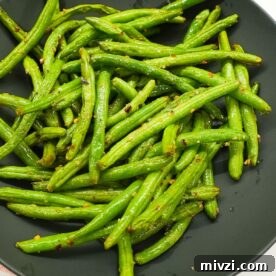 Crispy Air Fryer Green Beans with Garlic and Parmesan 4 Air fryer green beans in a bowl with visible garlic, red pepper flakes, and lightly blistered edges.