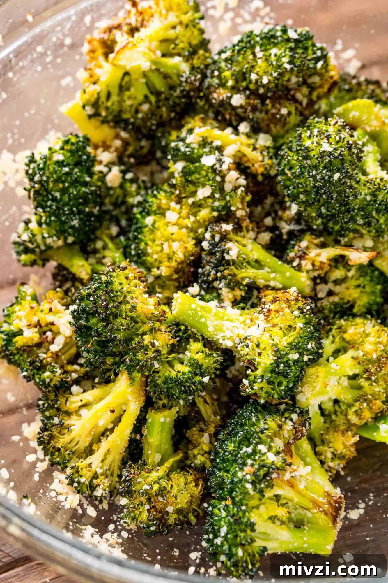 Roasted broccoli in a bowl being tossed with Parmesan.