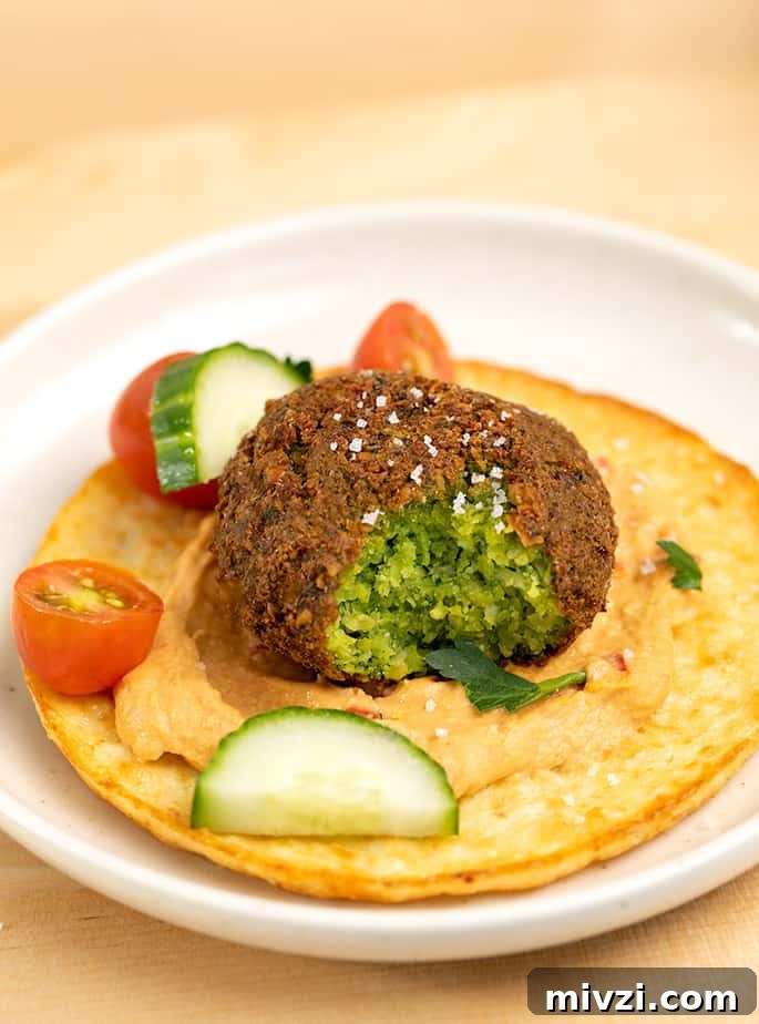 Falafel with bite taken on hummus with cut vegetables and herbs