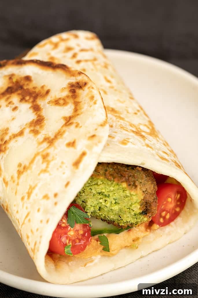 Falafel sliced in half with tomatoes and hummus in flatbread on small white plate