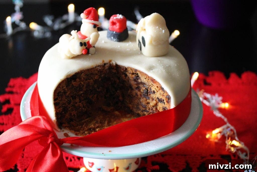 Dairy-Free Gluten-Free Christmas Cake Recipe 2 An iced Gluten Free Christmas Cake on a stand and surrounded by festive decorations. Several slices have been removed to show the dark fruity interior of the cake.
