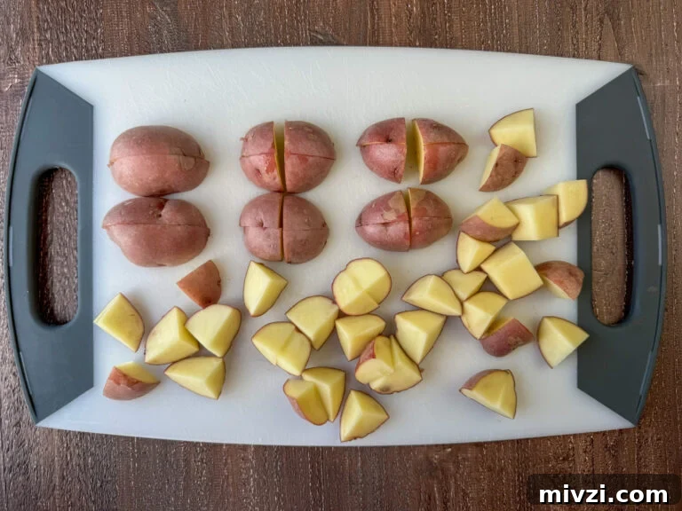 Red potatoes on a cutting board showing steps to cut into chunks to roast.